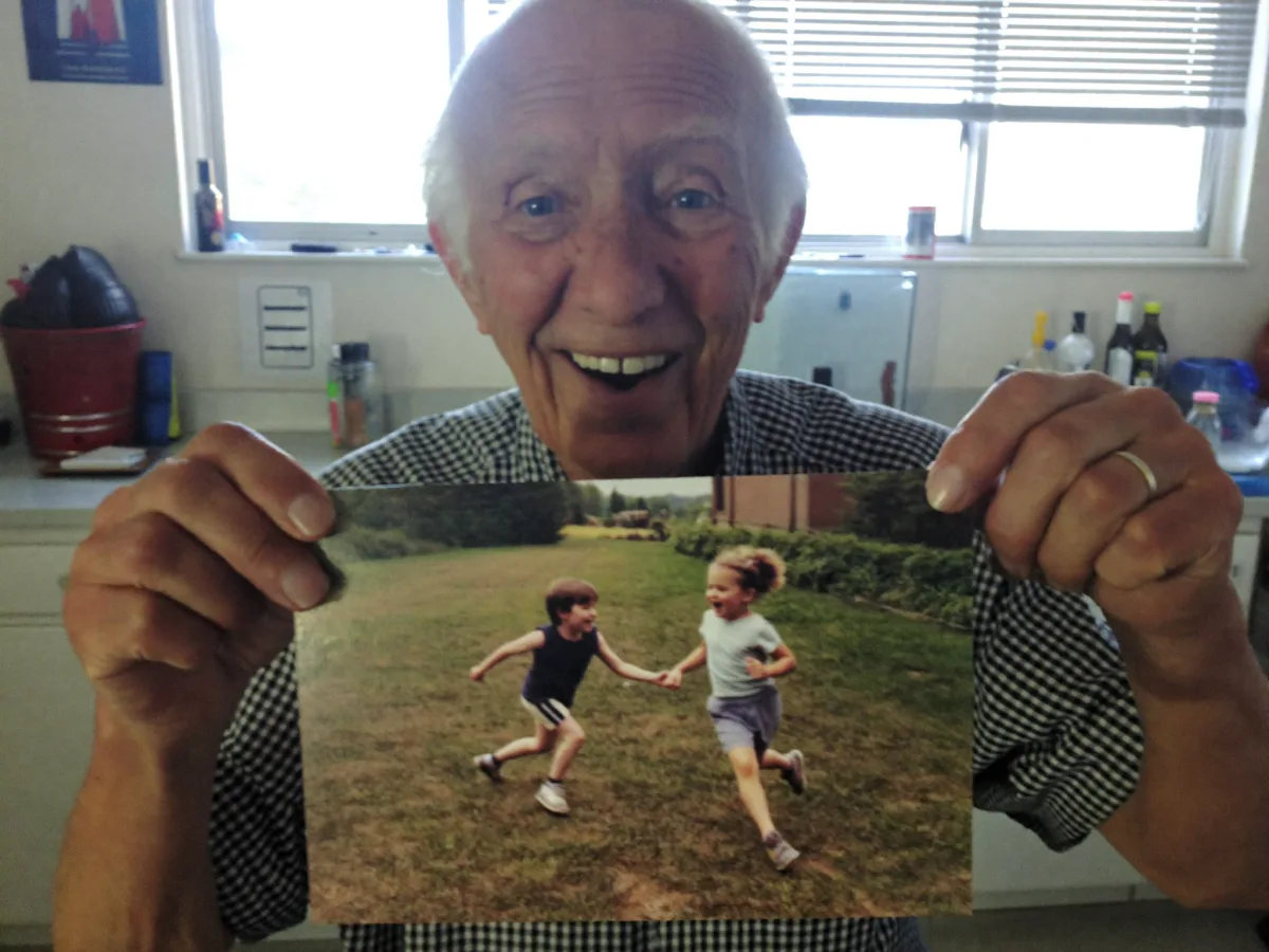 A delighted grandfather holding up a postcard with a family photo